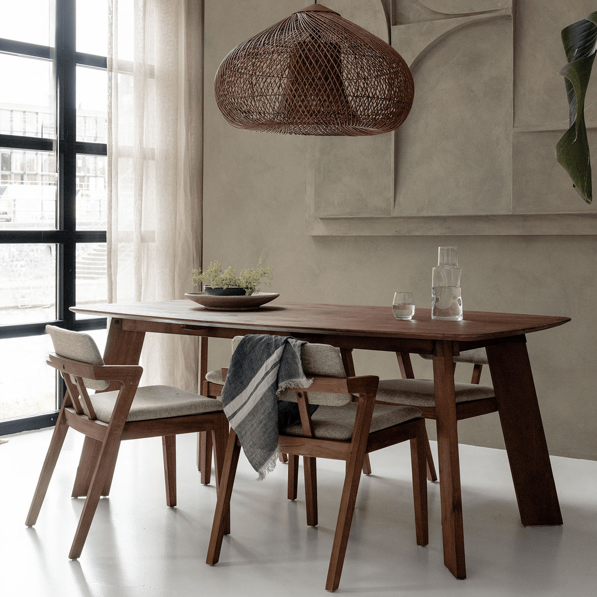 a wooden dining table and chairs in a room with a hanging rattan lampshade and floor to ceiling windows